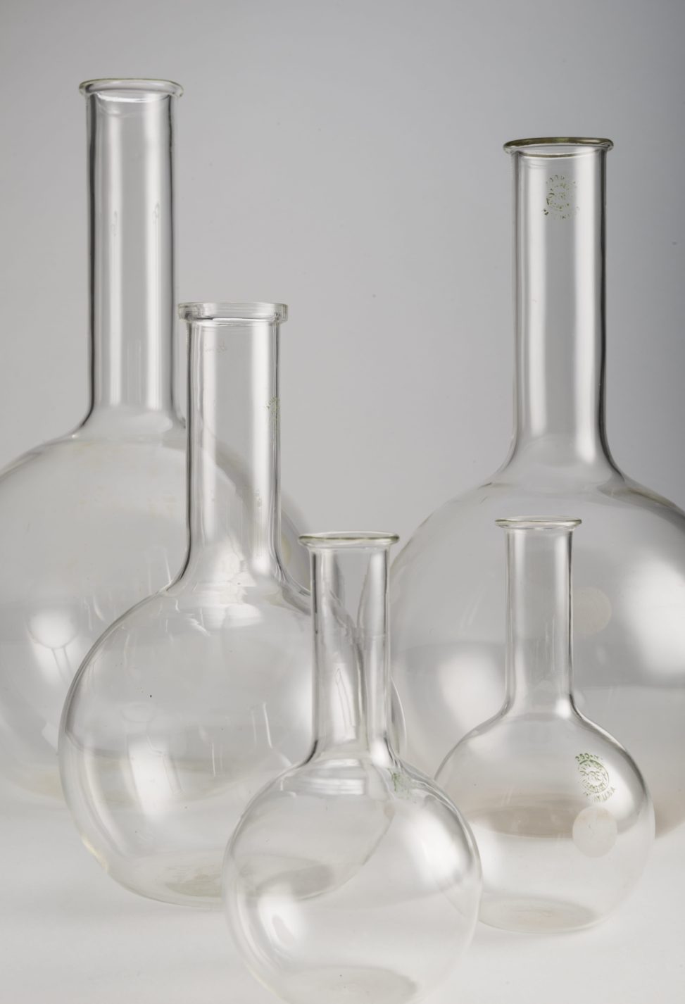 Cinq ballons de laboratoire à fond plat, tous en verre transparent, dotés d’une base sphérique et d’un col cylindrique. Deux ballons de 250 ml, un de 1L, un de 2L et un de 3L