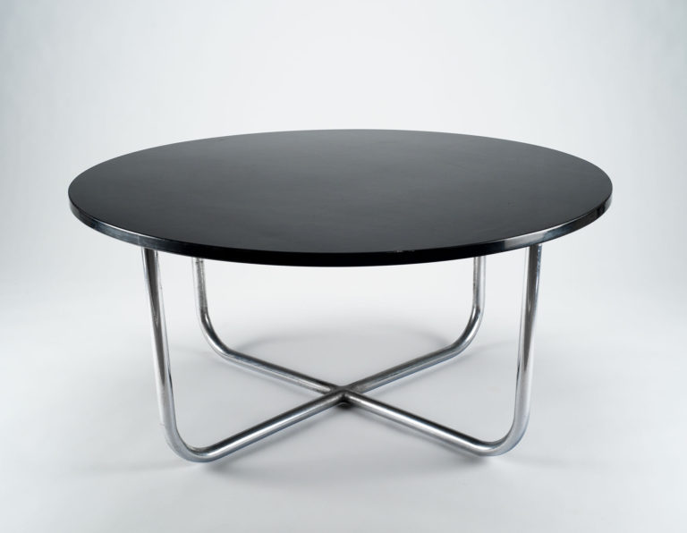 Coffee table. Circular black table top set on tubular steel legs that bend at the bottom and meet to form a cross at the center.