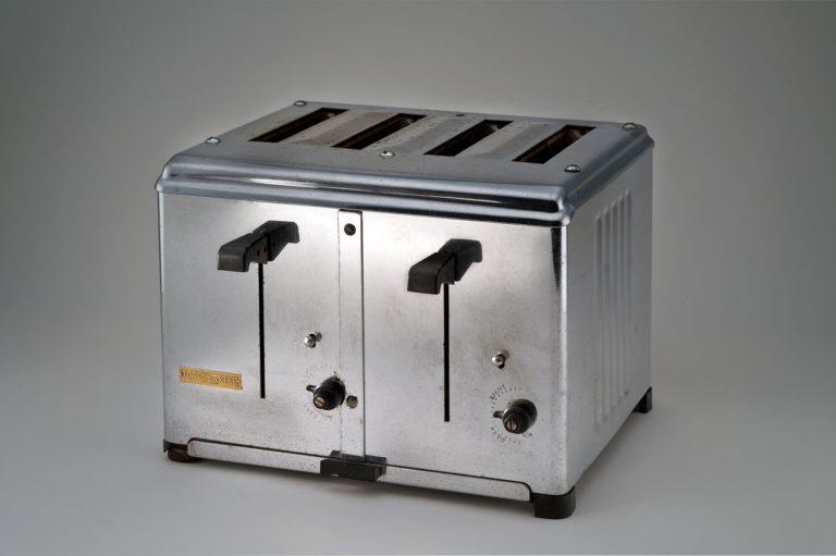Box-shaped shiny metal toaster with openings for four slices of bread. It has two levers and two control knobs in black plastic on the front.