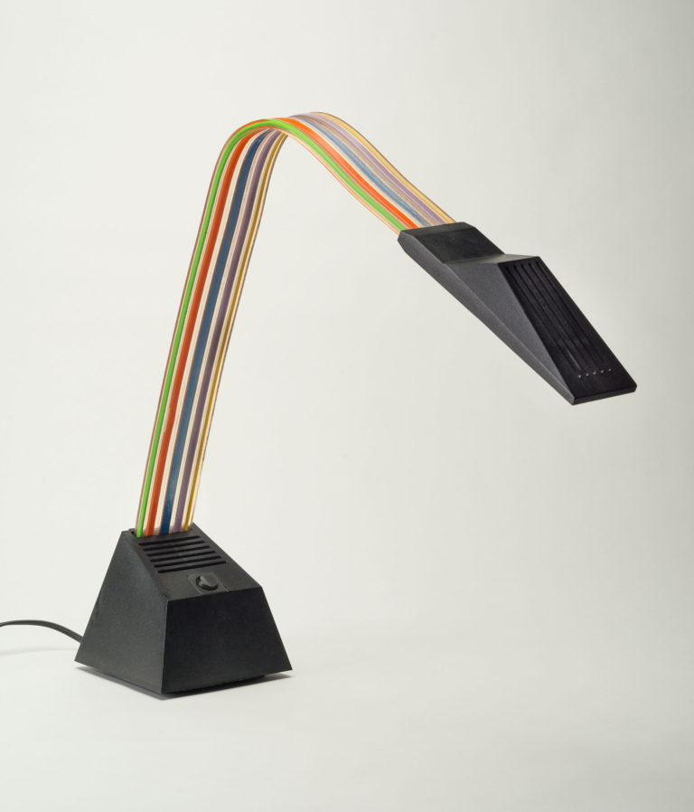 Table lamp with black metal base supporting a multicolored ribbon-like plastic shaft and black metal light casing.