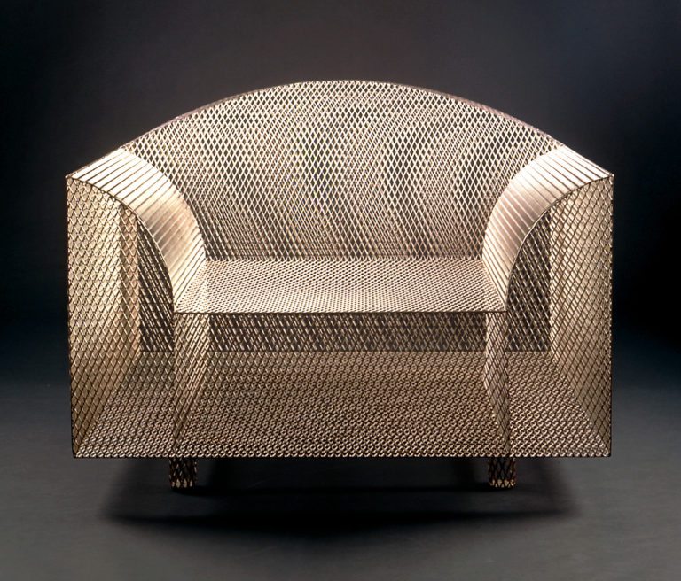 Armchair of metal mesh with rectangular base and curved arms and back.
