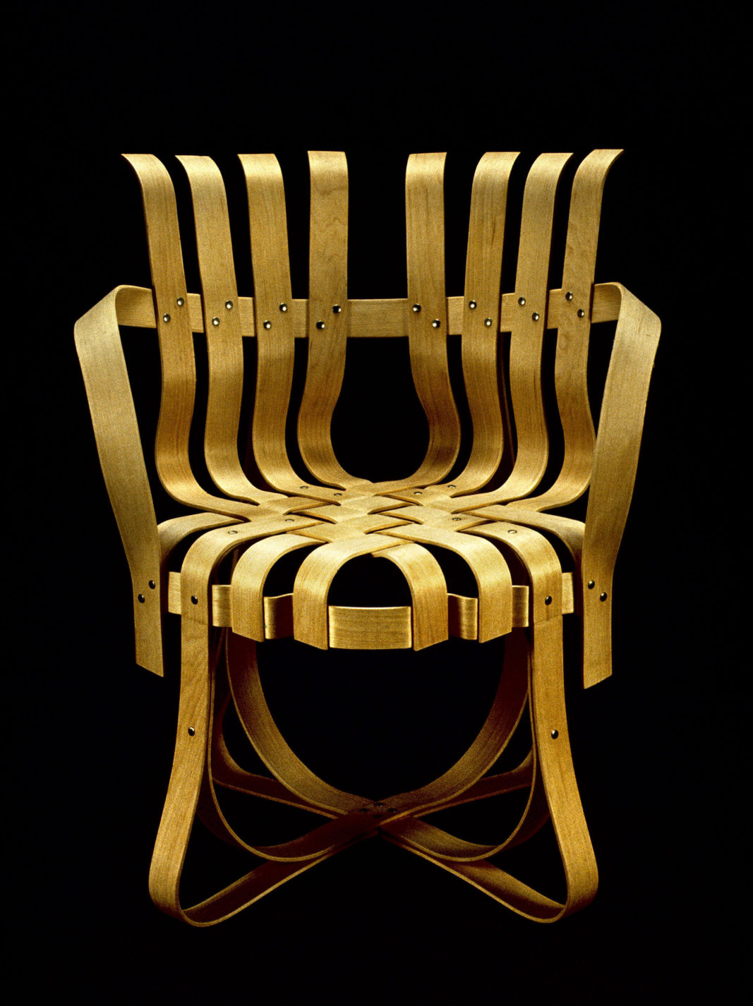 Armchair composed of numerous plywood strips bent to form curving arms, back, and legs, and woven together to form the seat.