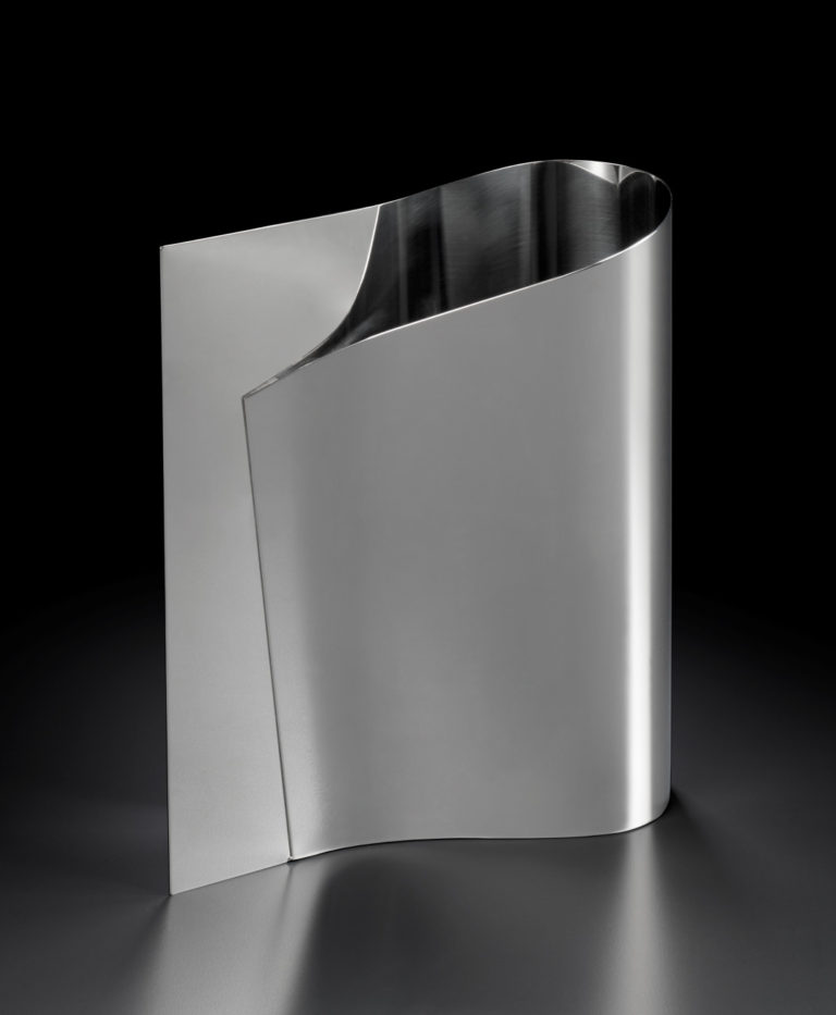 Vase. The two ends of a sheet of steel have been brought together on one side, leaving a rounded opening on the other.
