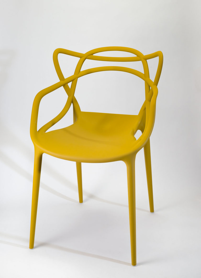 Plastic armchair in mustard yellow, with slender legs, solid seat, and open-frame back and arms.