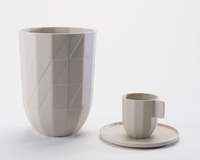 Large mug, small coffee cup and saucer. Each piece is beige porcelain and made to look like it is made of folded paper.