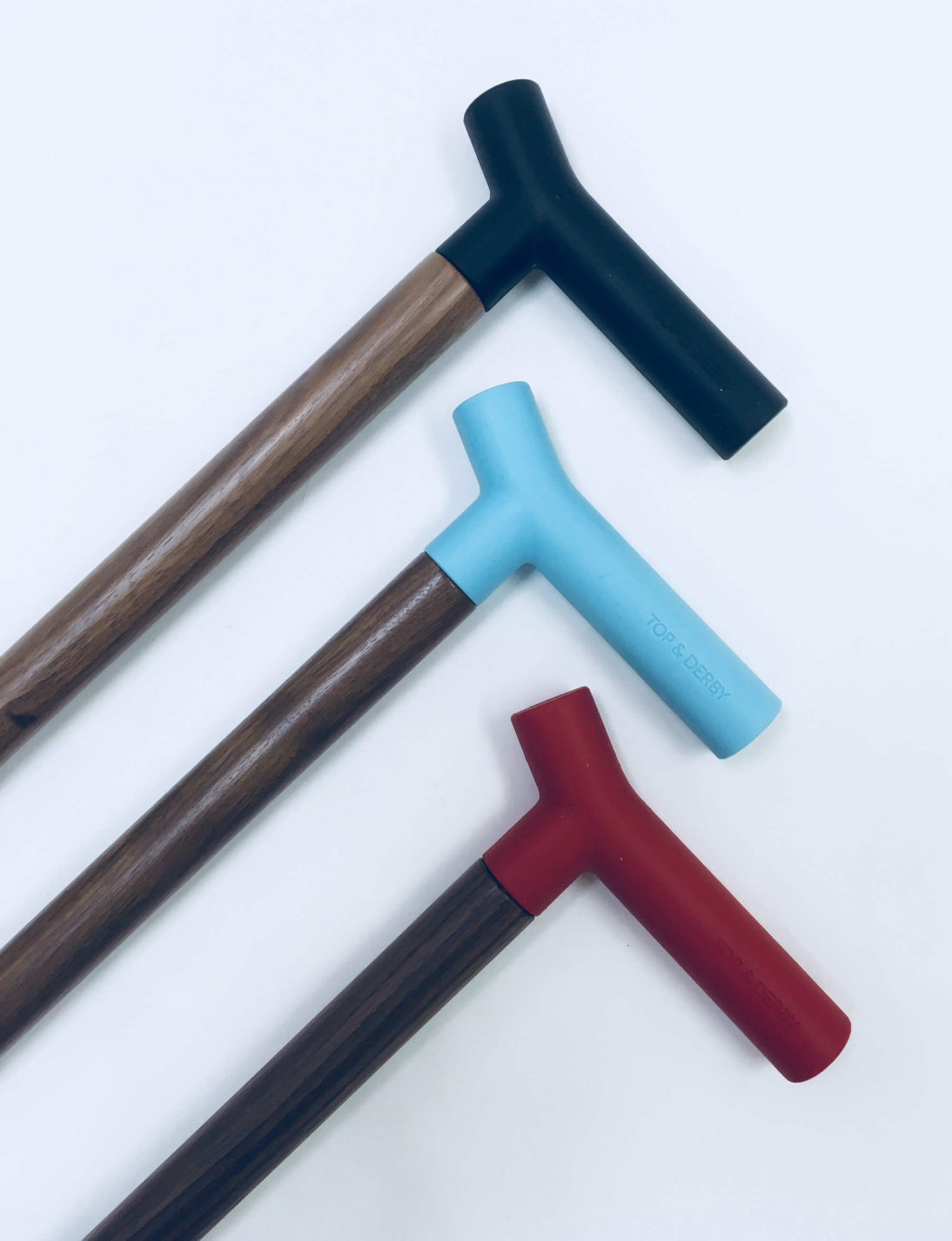 Trois cannes de marche en bois de différentes tailles à poignée en silicone noire, rouge ou bleu pâle.