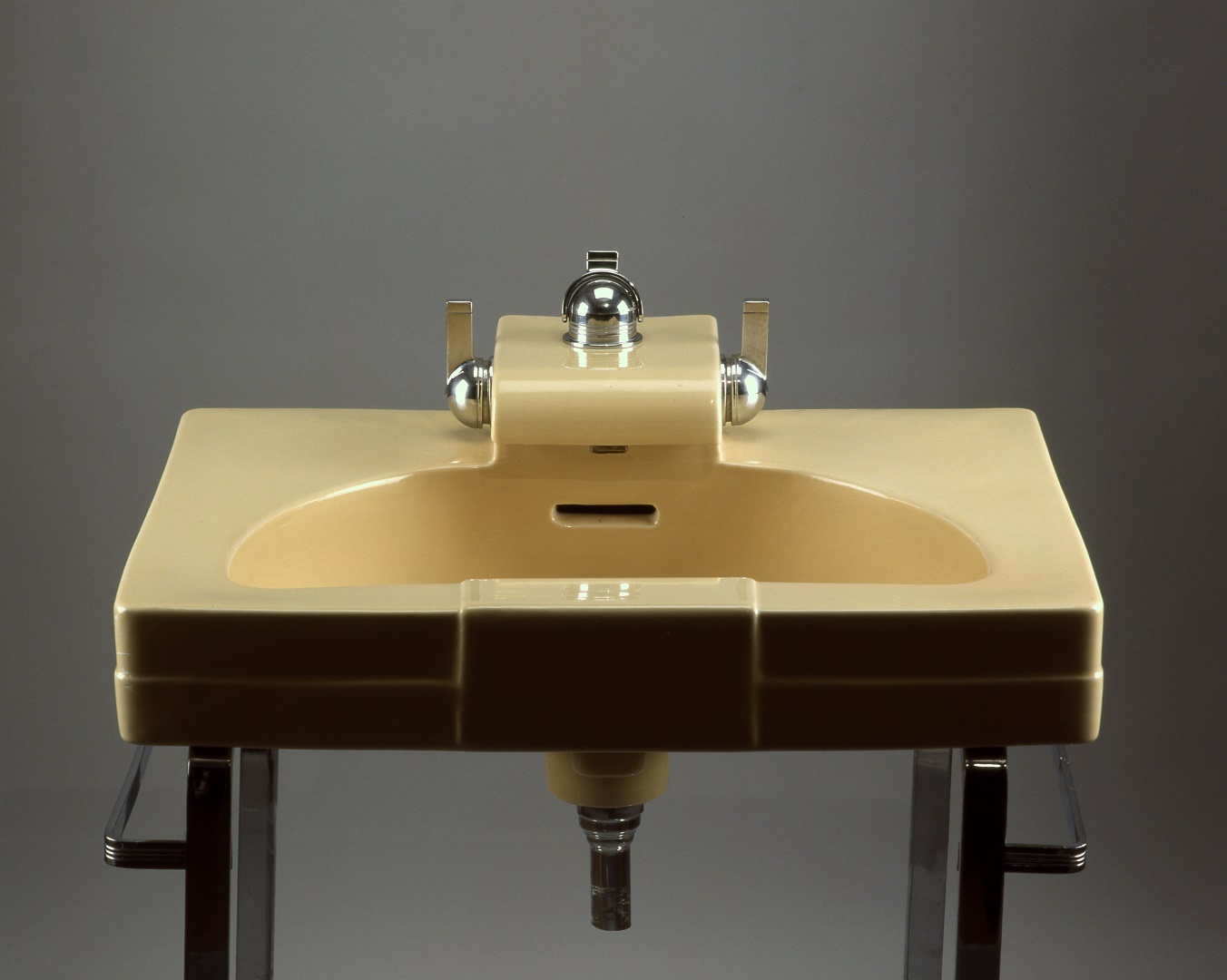 Rectangular bathroom sink with semicircular basin and dome-shaped shiny metal fixtures set on a stand of strap steel.
