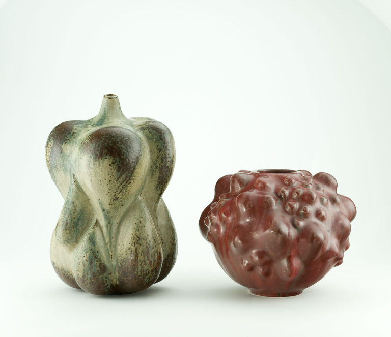 Two earthenware vases in organic forms. One in green resembles an assemblage of flower bulbs. The other in dark red has a bumpy surface like a gourd.