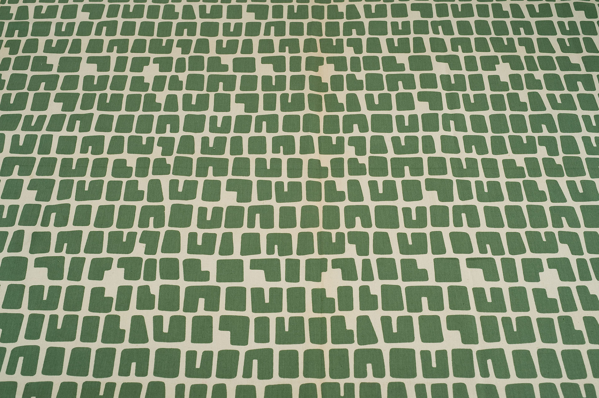 White textile with horizontal rows of blocky letter-like shapes in green.