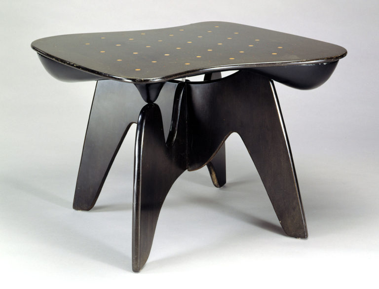 Low black table in wood with peg holes in the surface and curving sides and legs.