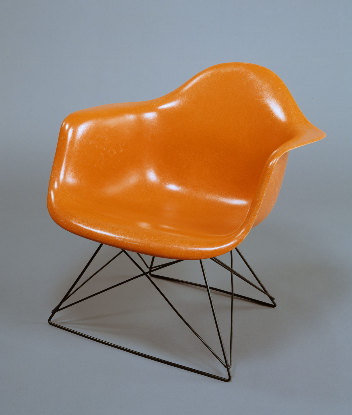 Large molded shell armchair in orange fiberglass with a crisscrossing base of black wire.