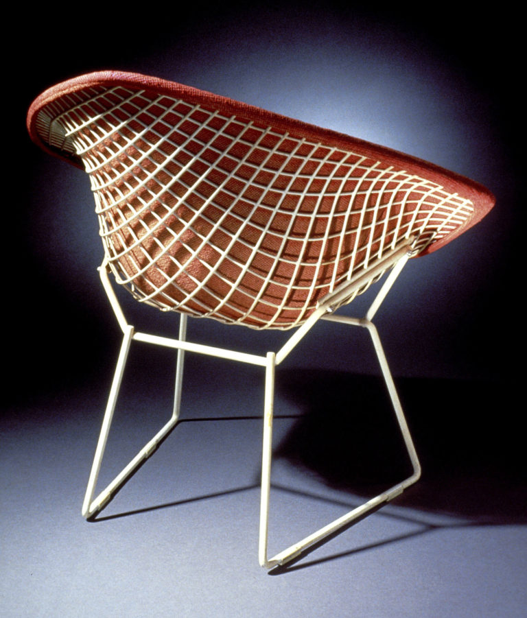 White wire-framed armchair viewed from the back. Seat, back, and arms are formed from an open wire mesh and covered on the front with red upholstery.