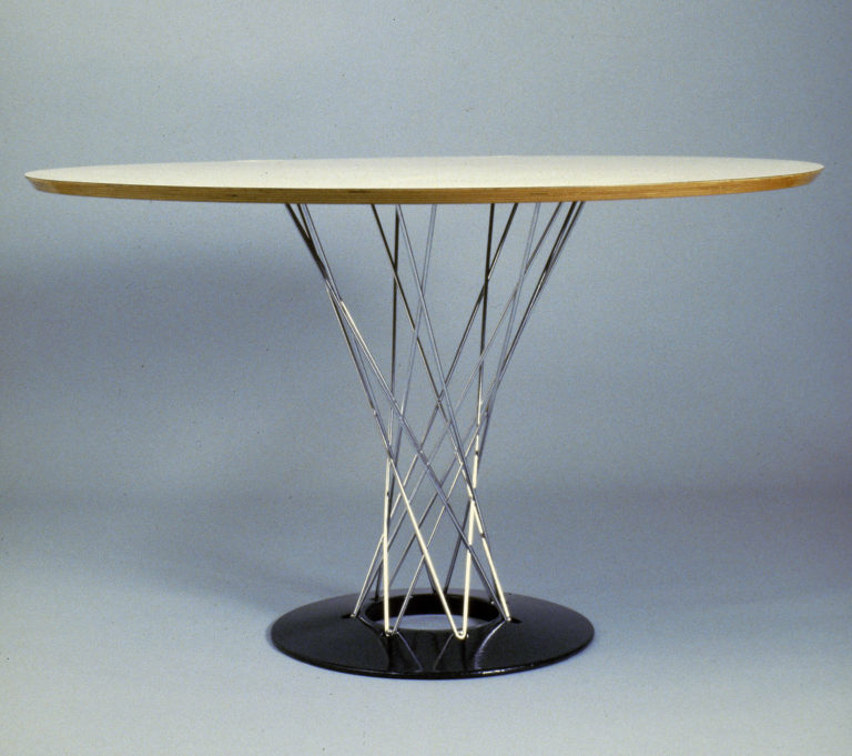 Circular table with white surfaced and wood-edged top on a crisscrossing steel wire and black disc base.