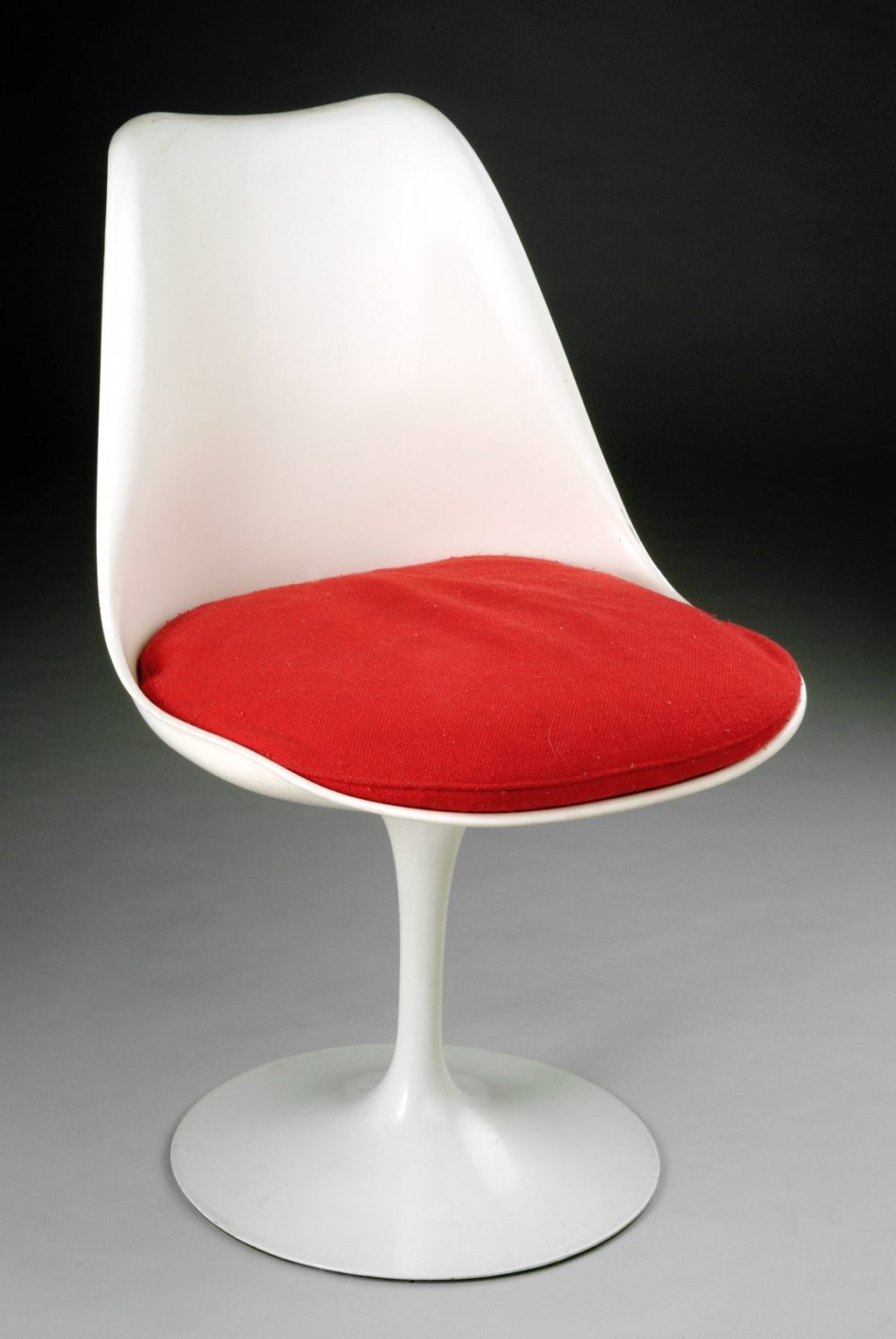 White plastic shell chair with a red cushion supported by a slender stem and a flared circular base.