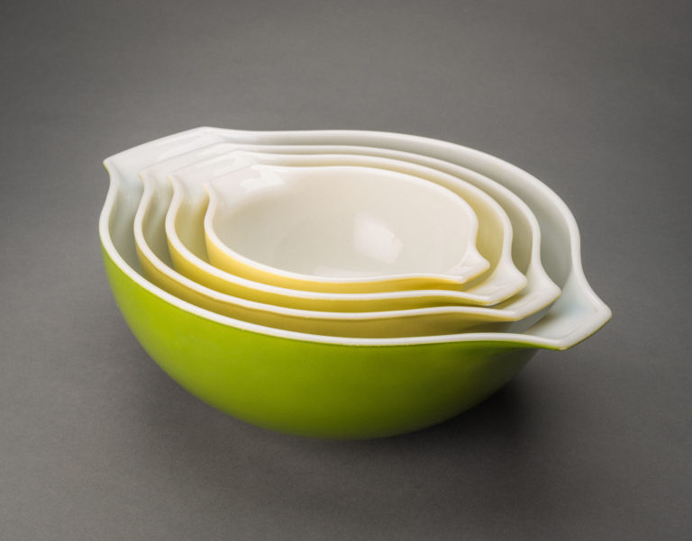 Set of four glass mixing bowls nested together. Each bowl has a white interior. The exterior colors, from smallest bowl to largest, are yellow, yellow-green, pale green, and medium green.
