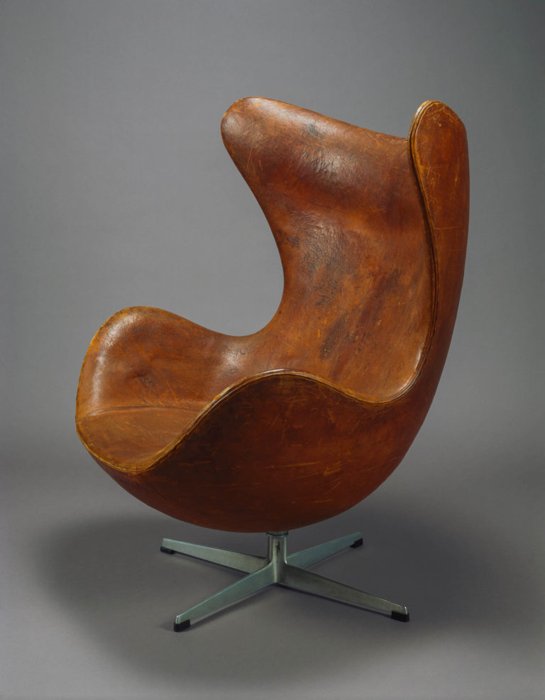 Armchair covered in brown leather as one shell with an X-shaped metal base.