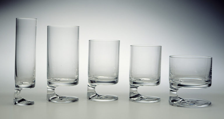 Five glasses in gradating sizes, each a cylindrical form with stem set on one side above a circular base.
