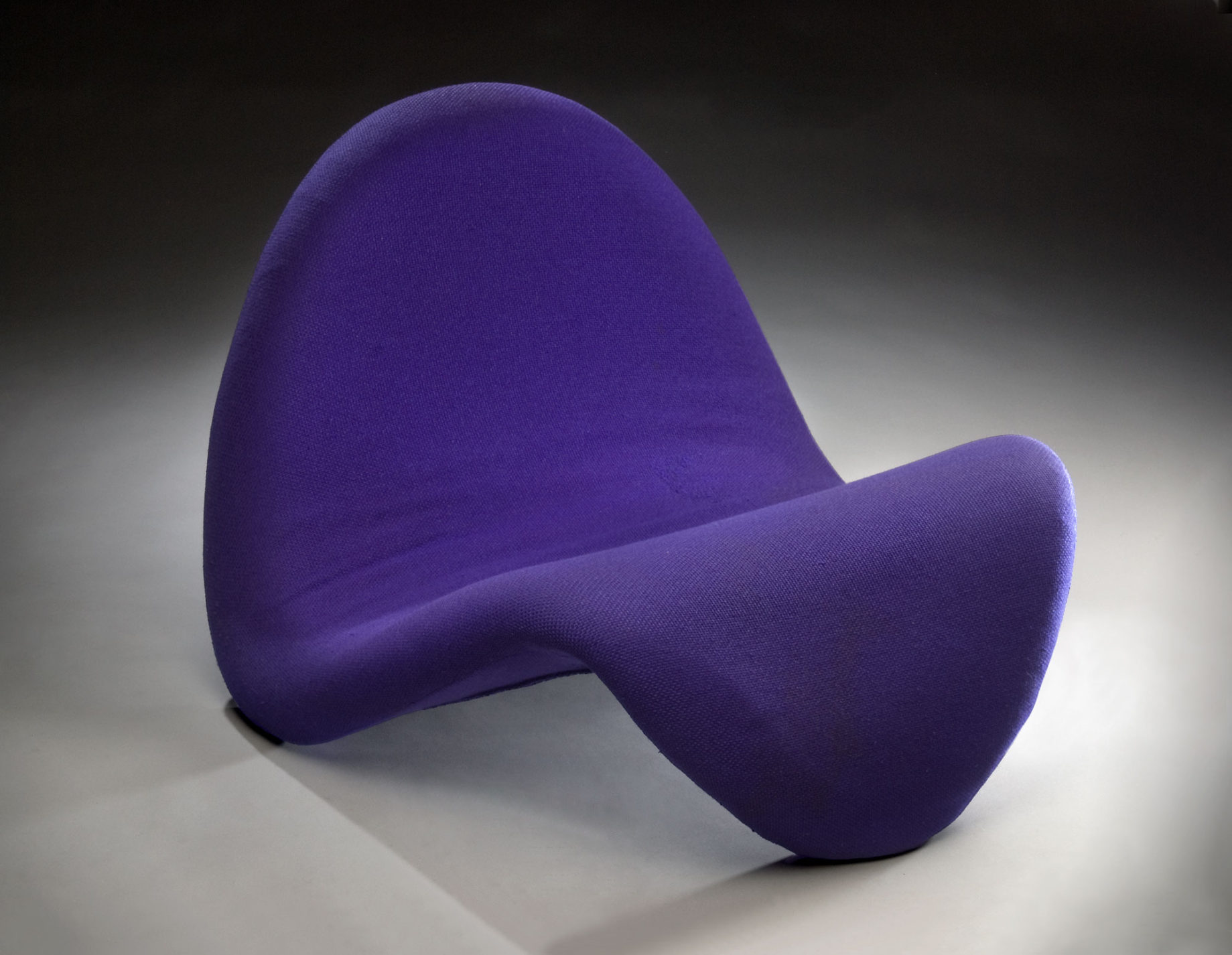 Curved lounge chair, back and front composed of a single undulating form covered in purple upholstery.