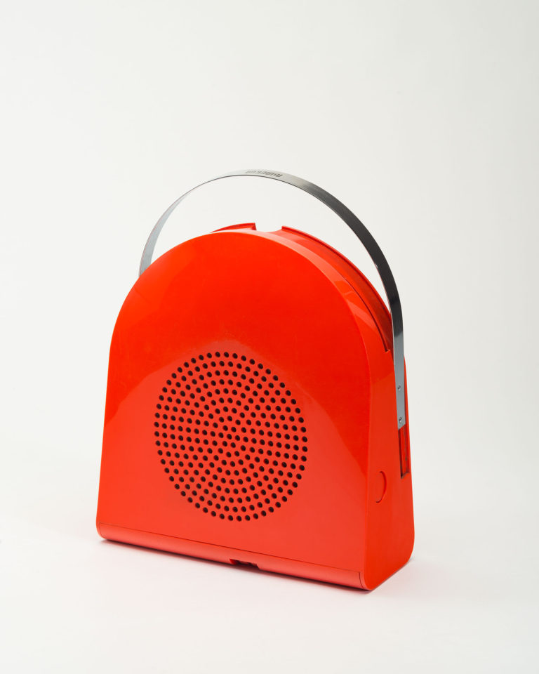 Tourne-disque voûté de plastique rouge avec poignée d’acier arrondie et rétractable sur le dessus. Un cercle perforé au centre sert de haut-parleur.