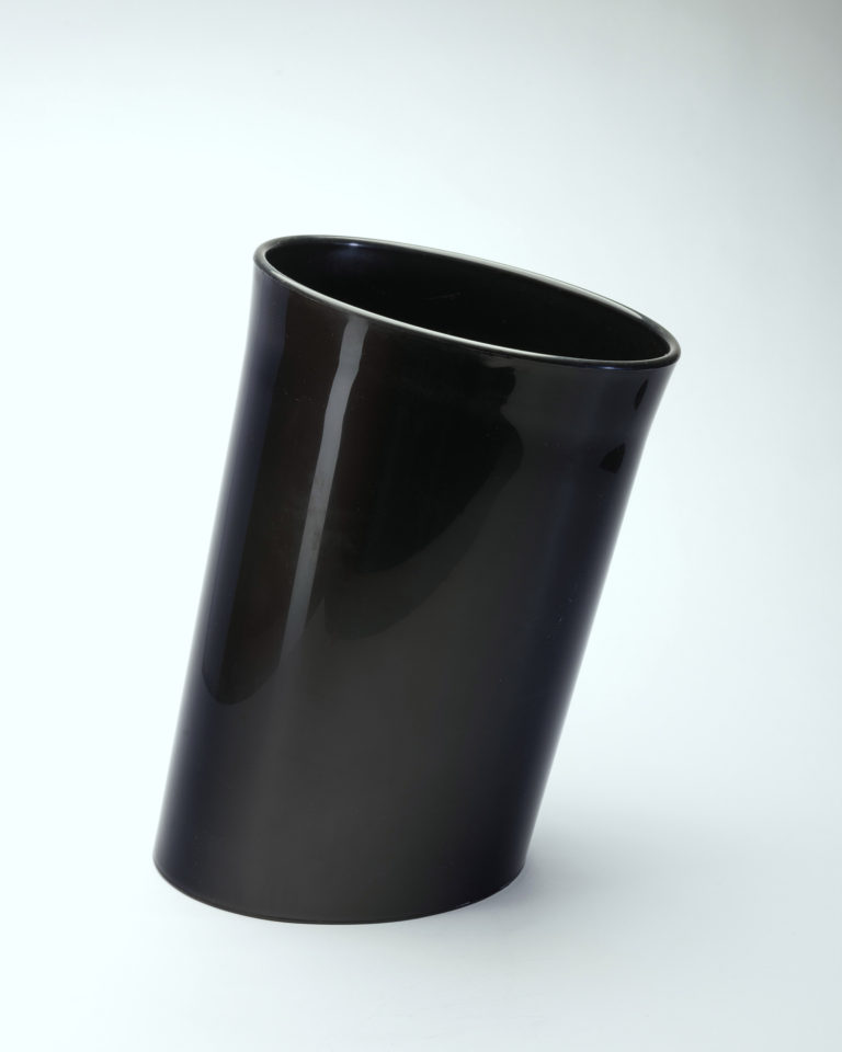 Slanted cylindrical waste basket in black plastic.