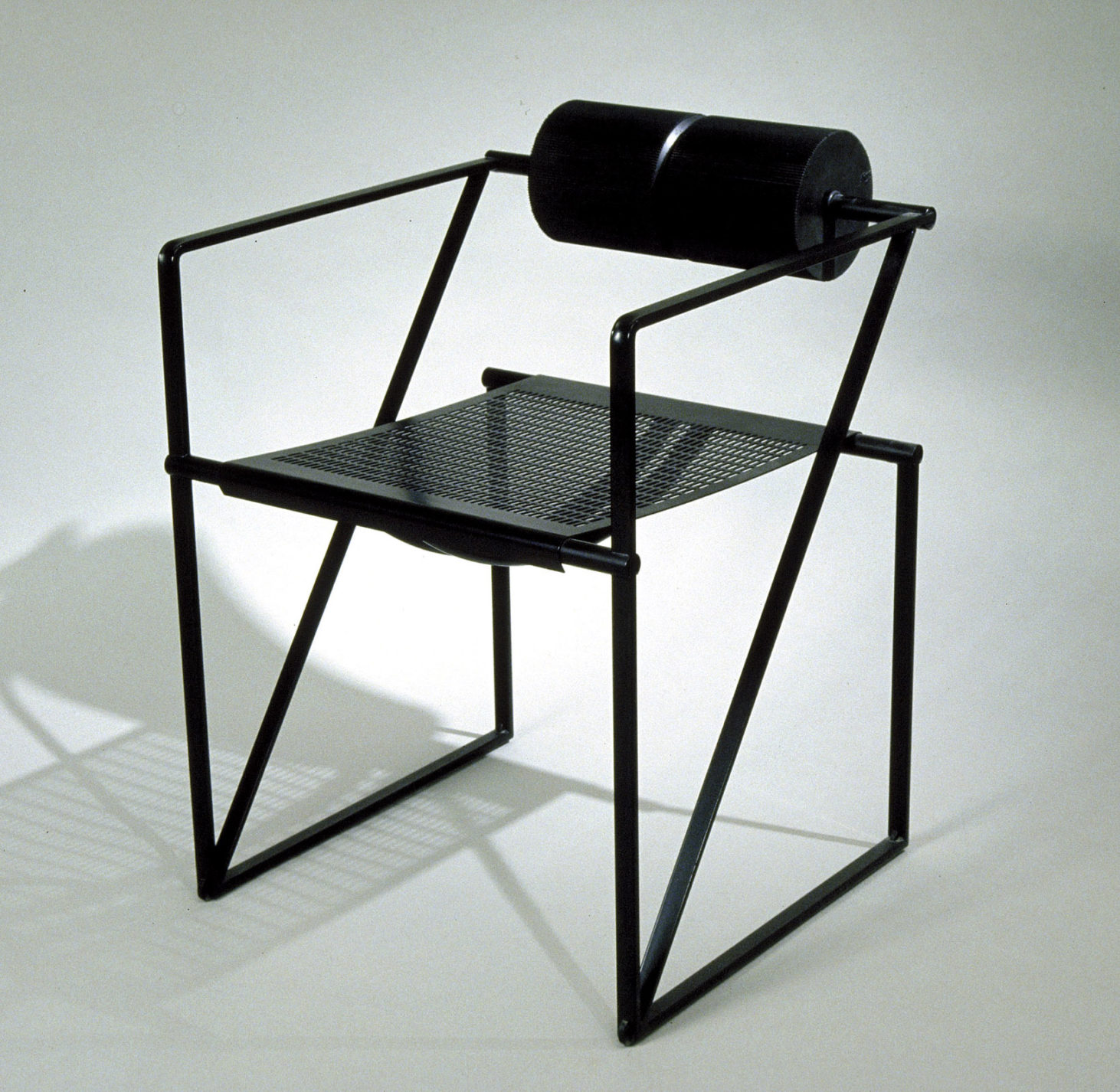 Fauteuil noir au cadre profilé en acier tubulaire muni d’une assise en métal et d’un coussin cylindrique en guise de dossier.