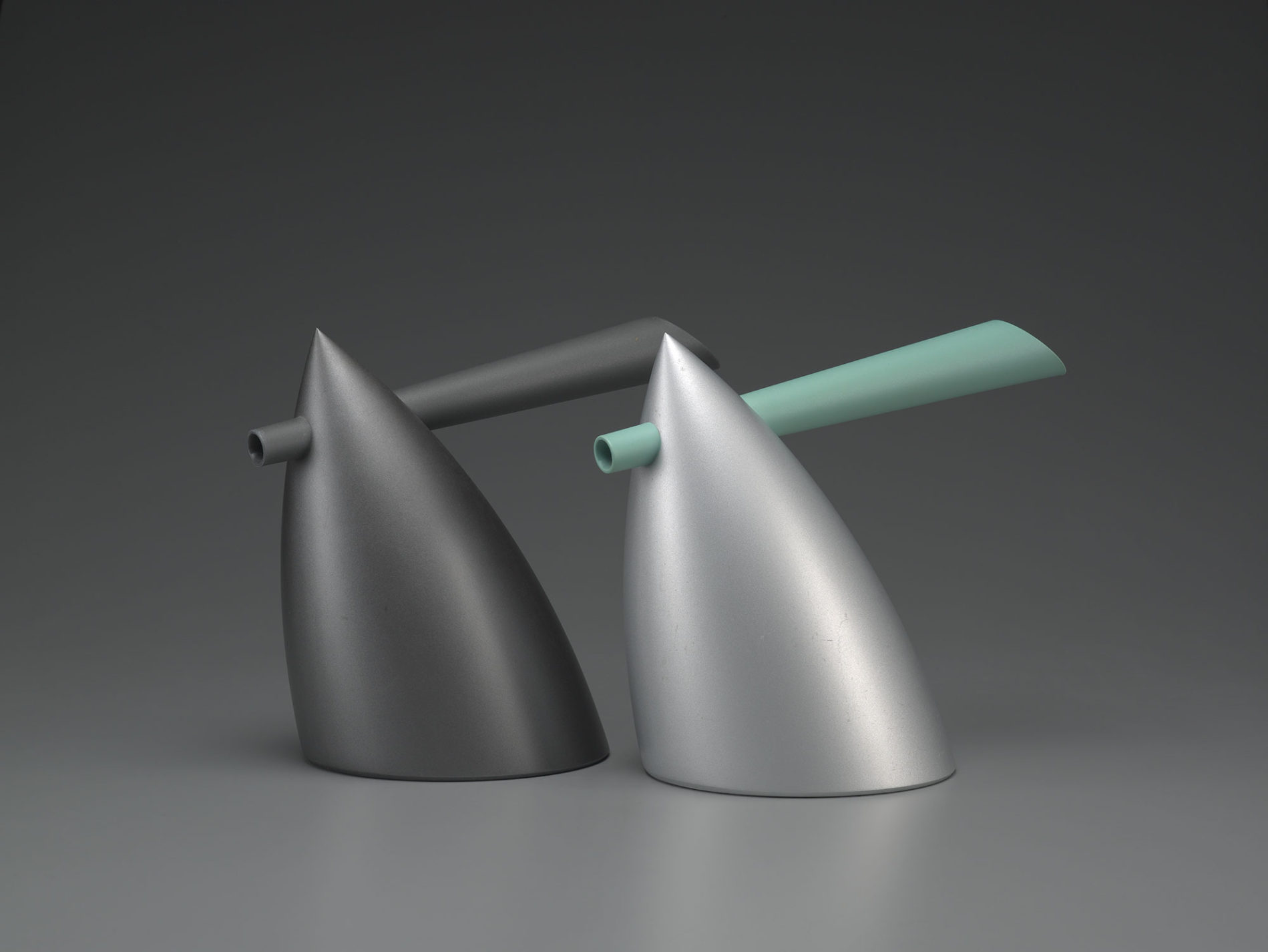 Two bullet-shaped kettles with a combined spout and handle that goes through the point at the top. One is all dark grey, the other is light gray with a pale blue-green spout/handle.