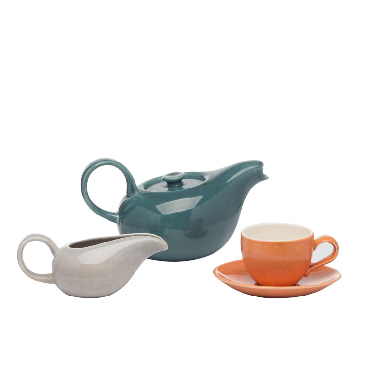 Ceramic dishes. Dark green teapot with elongated spout and rounded handle, elongated grey creamer with open spout and rounded handle, and simple coral-colored teacup with saucer and off-whited cup interior.