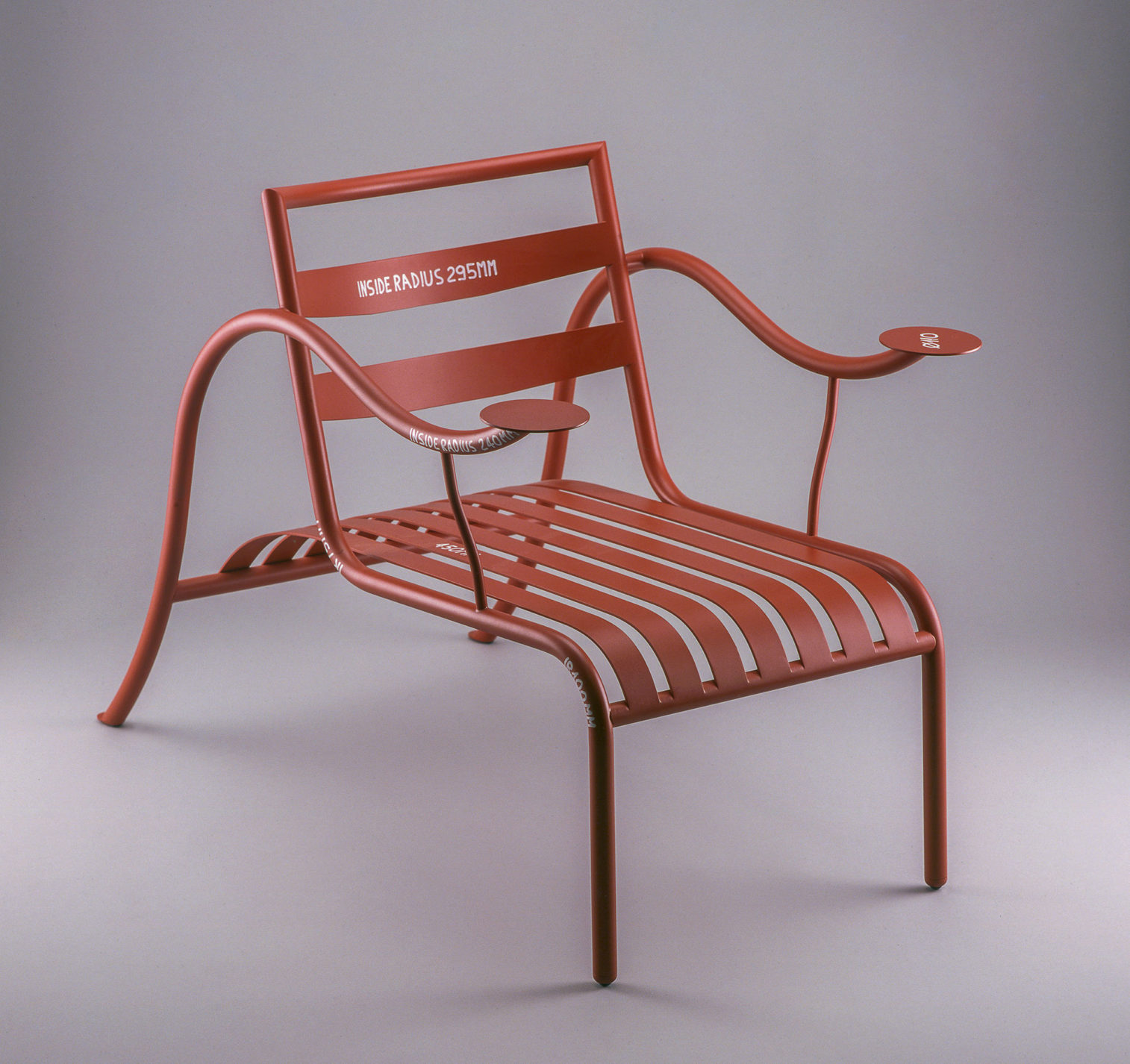 Rust-colored lounge chair in painted steel with curved horizontal back slats. Steel-slat seat extends to curved tubular-steel rear legs, which continue in a single piece to form undulating arms with circular disks at each end.