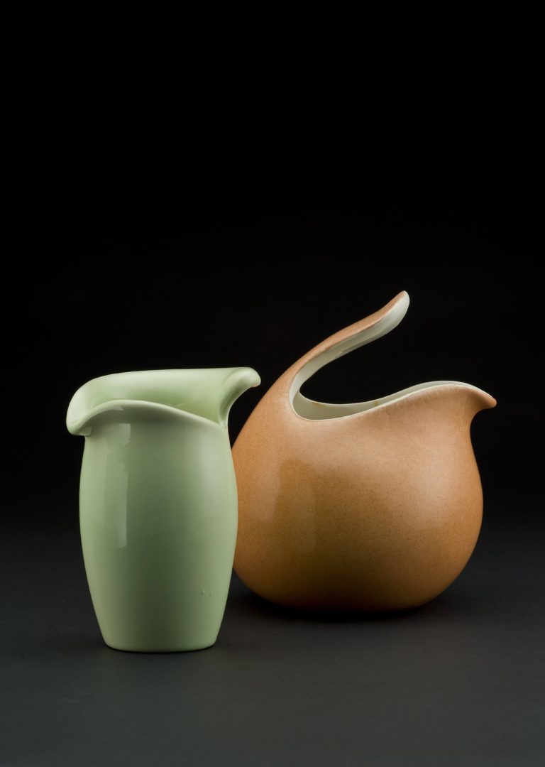 Two ceramic vessels. One pale green, slightly bulbous cylinder with a leaf-like opening at the top, the other terra-cotta colored spherical shape with a handle protruding over the opening at the top.